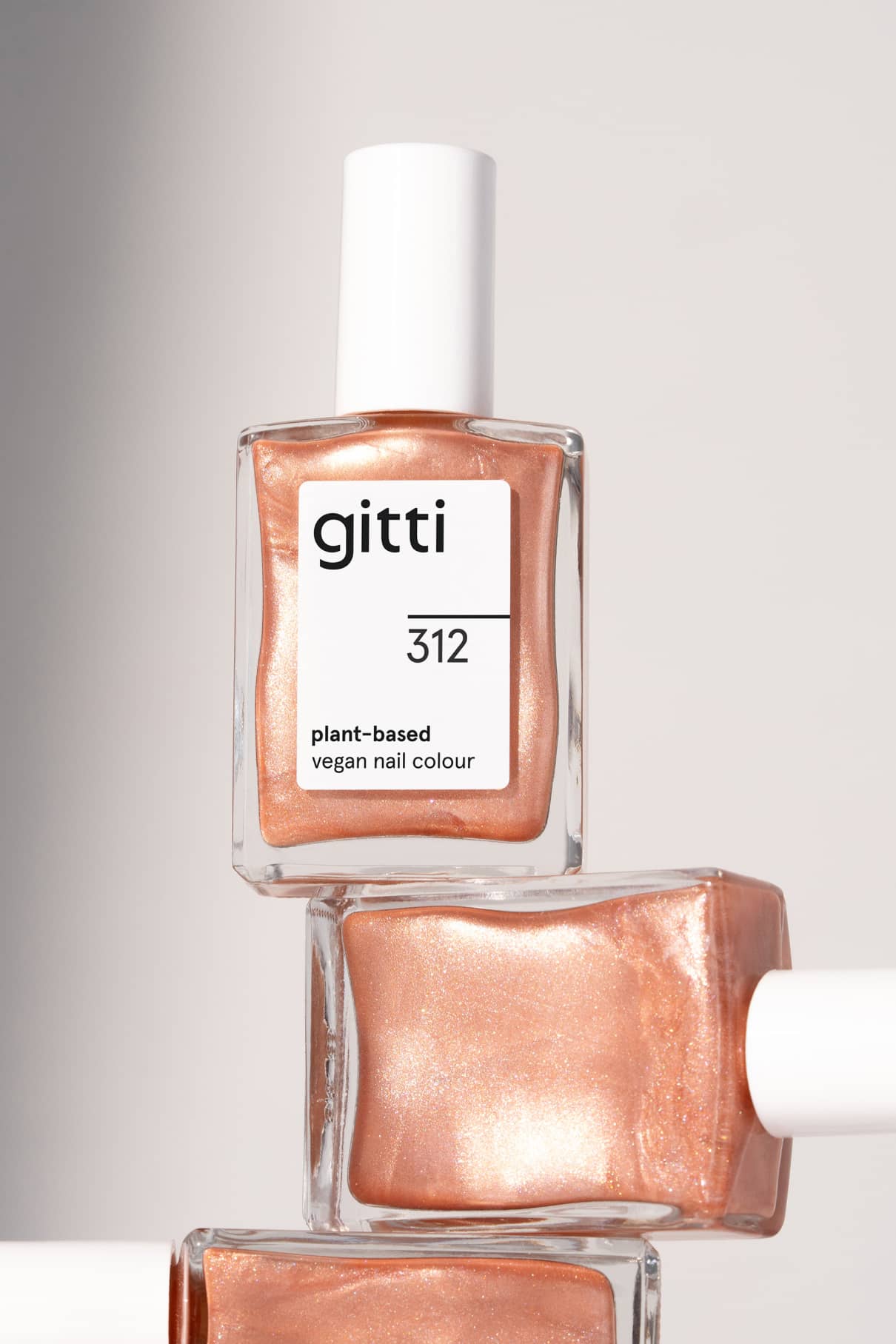 Drei Flaschen von gitti no. 312, ein veganer Nagellack auf pflanzlicher Basis in einem metallischen Apricot-Roségold-Ton, sind ordentlich vor einem neutralen Hintergrund gestapelt.