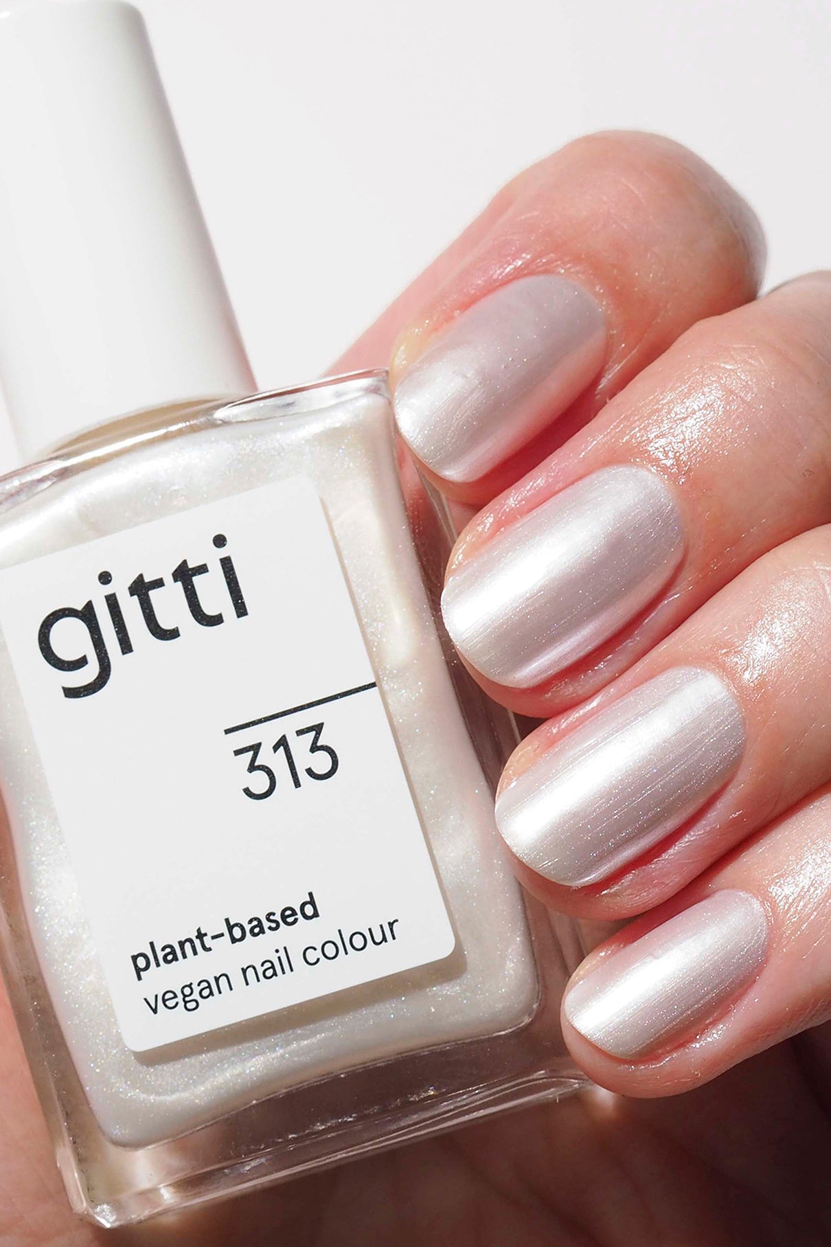Eine Hand mit Pearl Nails in Metallic-Weiß hält eine Flasche mit der Aufschrift gitti no. 313, eine pflanzliche, vegane Nagelfarbe - perfekt für Ihren nächsten Trend-Look.