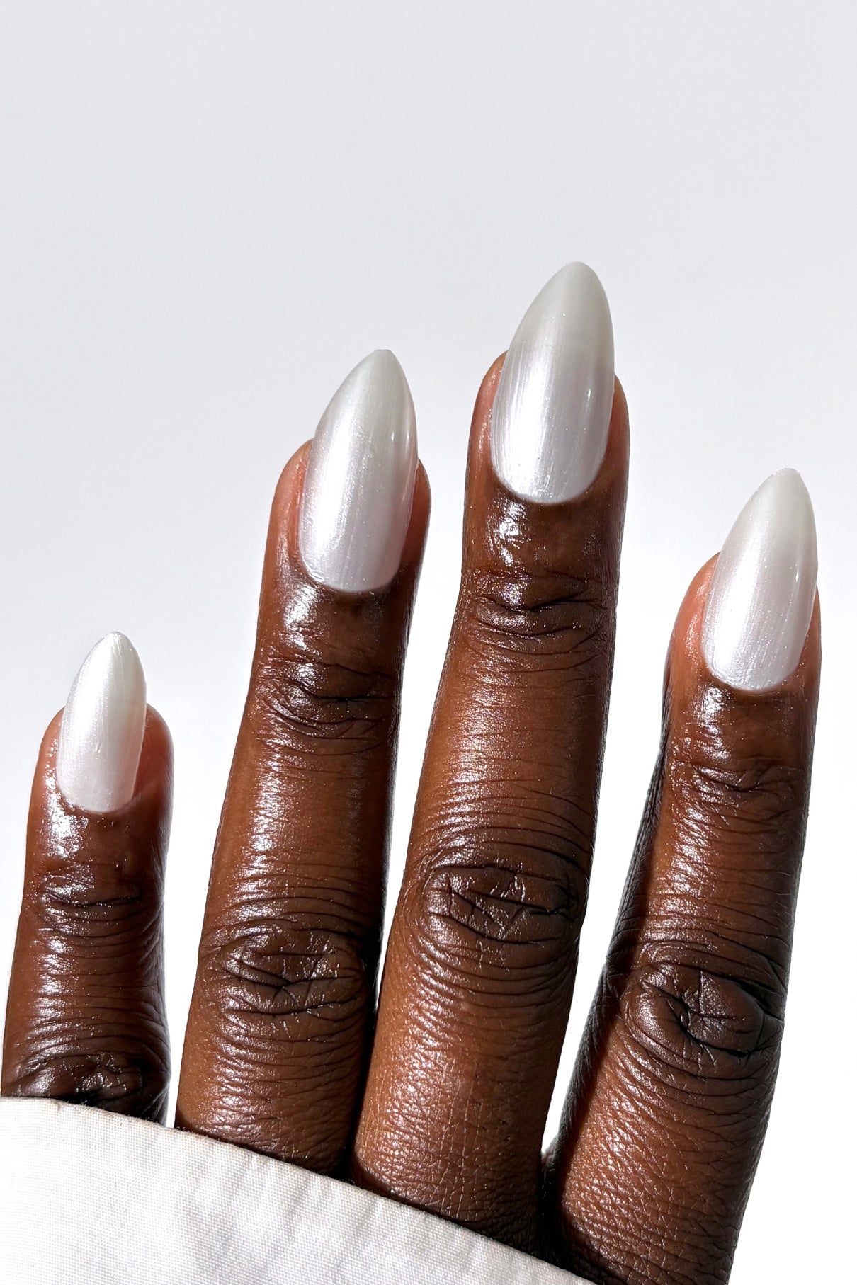 Eine Nahaufnahme einer Hand mit dunkler Haut und langen, mandelförmigen Nägeln, die mit gitti no. 313 lackierten Nägeln, die einen modernen Pearl Nails Trend-Look unterstreichen.