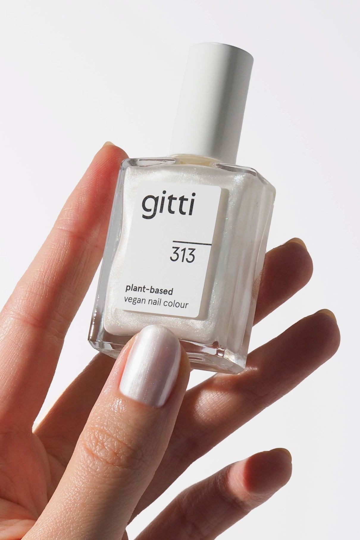 Eine Hand mit perlweißem Nagellack setzt die gitti no. 313, eine pflanzliche, vegane Farbe in Metallic-Weiß, die einen schicken Trend-Look vor einem knackigen weißen Hintergrund kreiert.