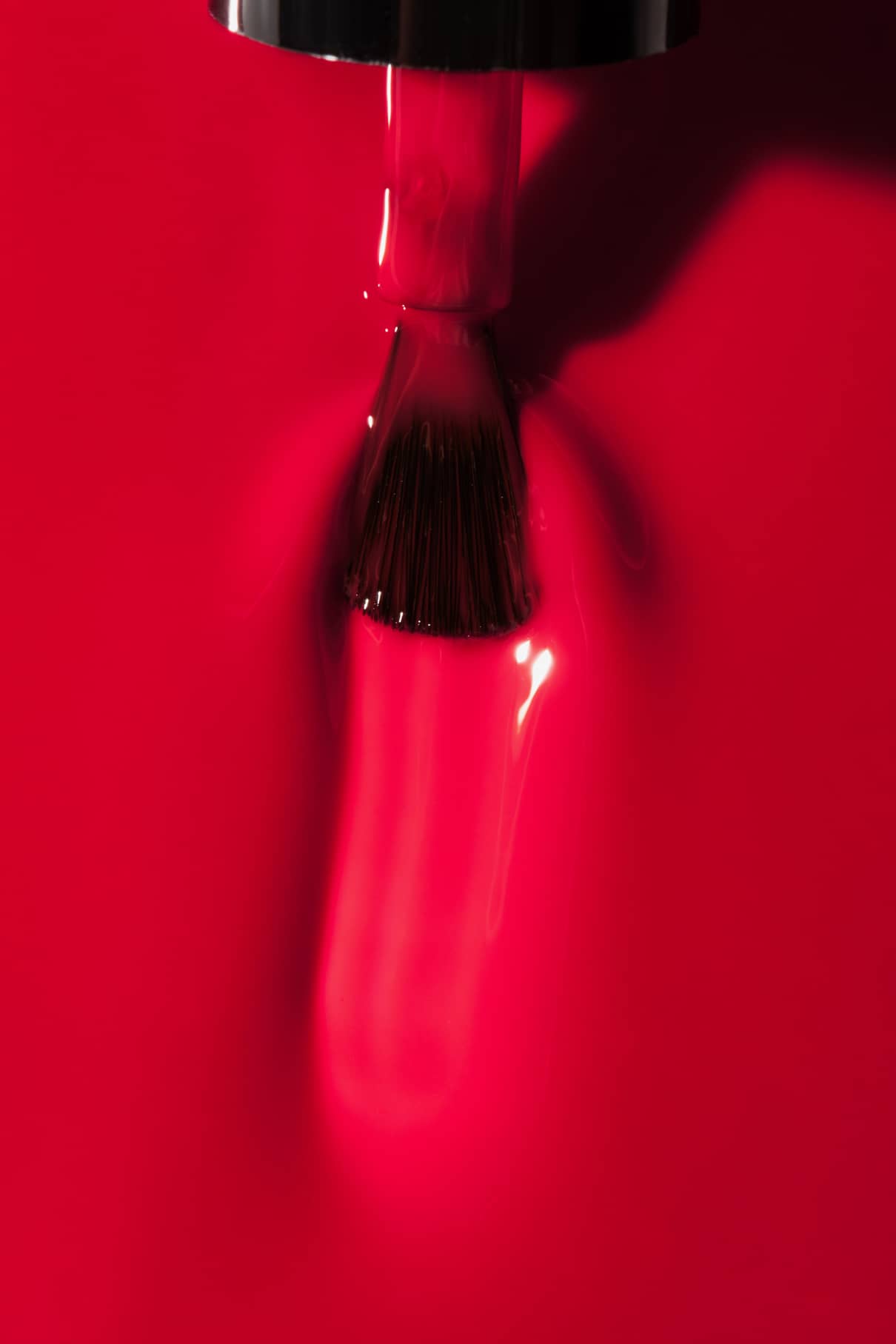Nahaufnahme eines Nagellackpinsels, mit dem gitti no. 01+, ein intensiv glänzender roter Nagellack, auf eine glatte Oberfläche.