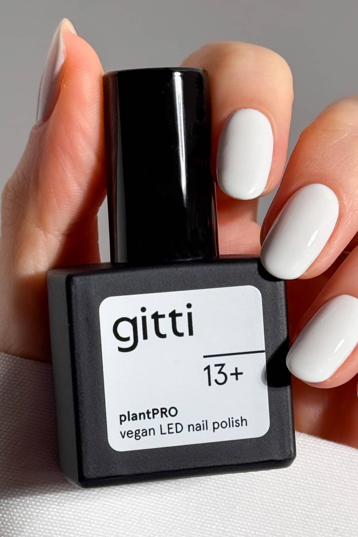 Eine Hand mit weiß lackierten Nägeln hält eine schwarze Flasche des veganen LED-Nagellacks gitti PRO Colour Trio, der Teil des plantPRO Farben Sets ist.