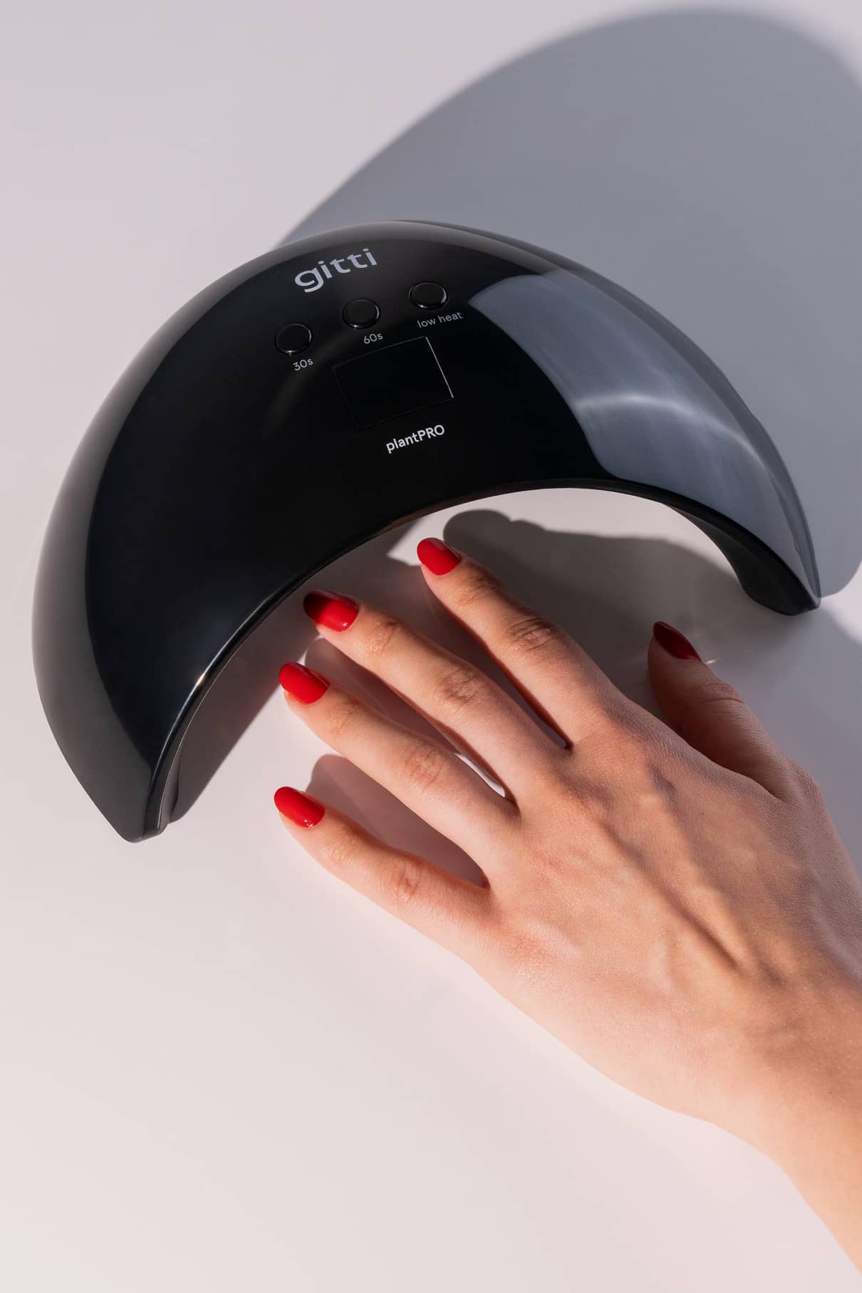 Eine Hand mit rot lackierten Nägeln wird unter der schwarzen plantPRO System + Lampe auf eine hellgraue Fläche gelegt.