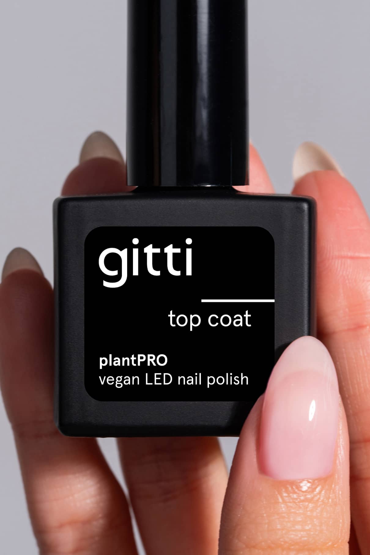 Eine Hand mit manikürten Gelnägeln hält eine schwarze Flasche mit der Aufschrift plantPRO Top Coat, einem veganen LED-Nagellack auf Pflanzenbasis von gitti.