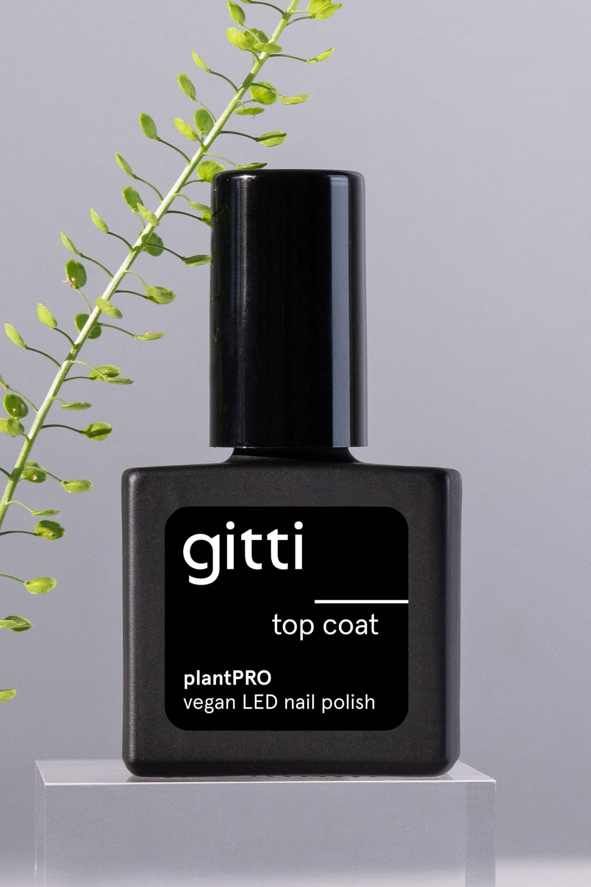 Eine schwarze Flasche plantPRO Top Coat ist mit einem grünen Pflanzenzweig im Hintergrund abgebildet, ideal für einen natürlichen Gelnagel-Look.