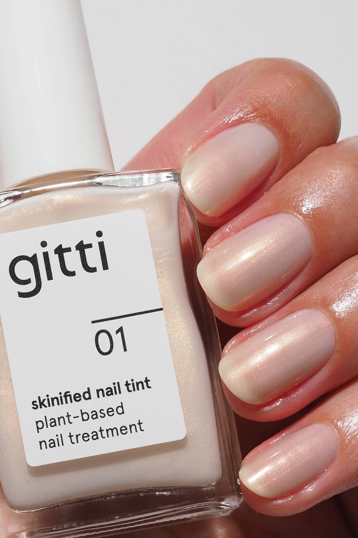 Close-up of a hand holding gitti Skinified Nail Tint 01 bottle with nude polished nails
