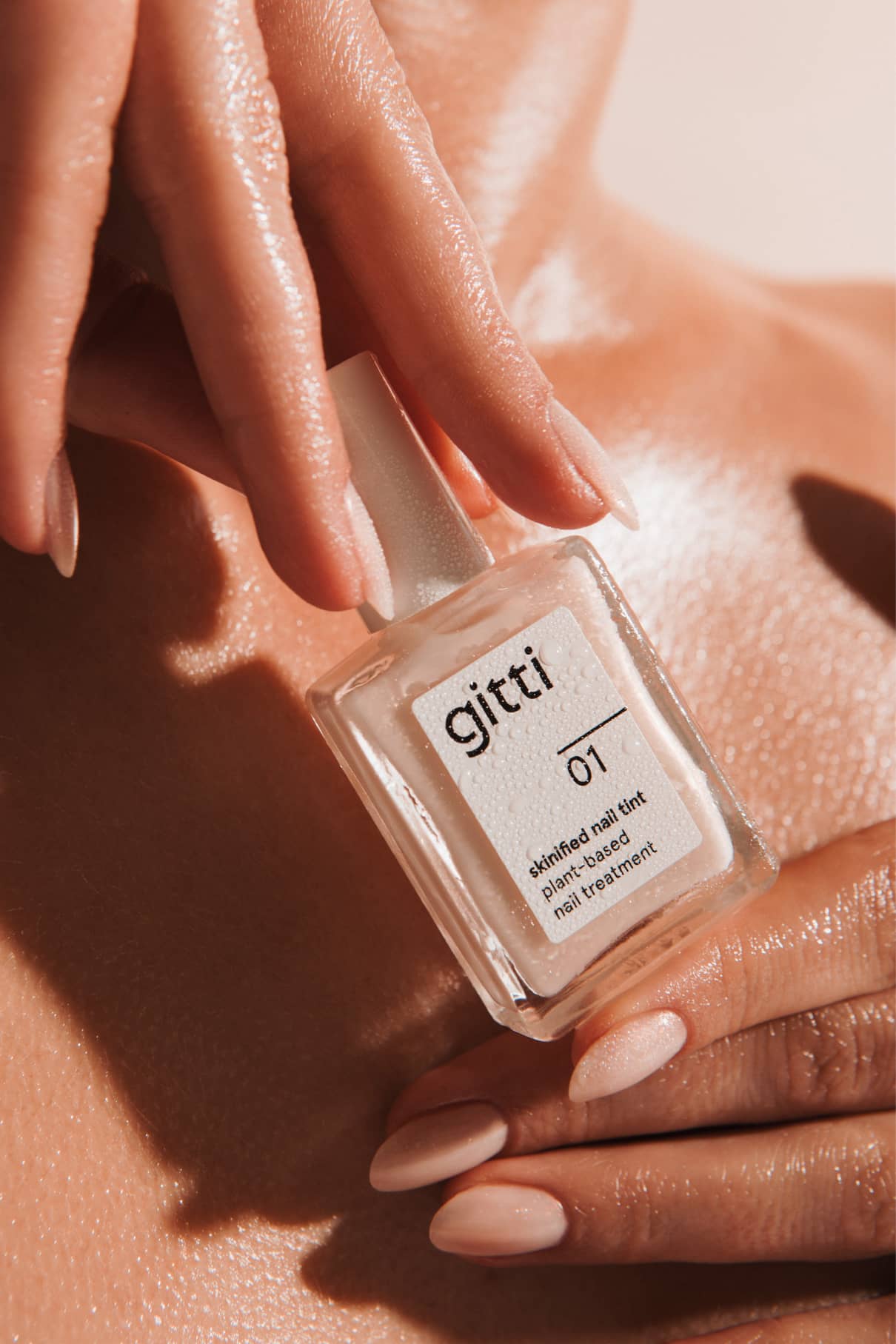 Close up of a hand holding a nail tint bottle with a white cap and nude polished nails
