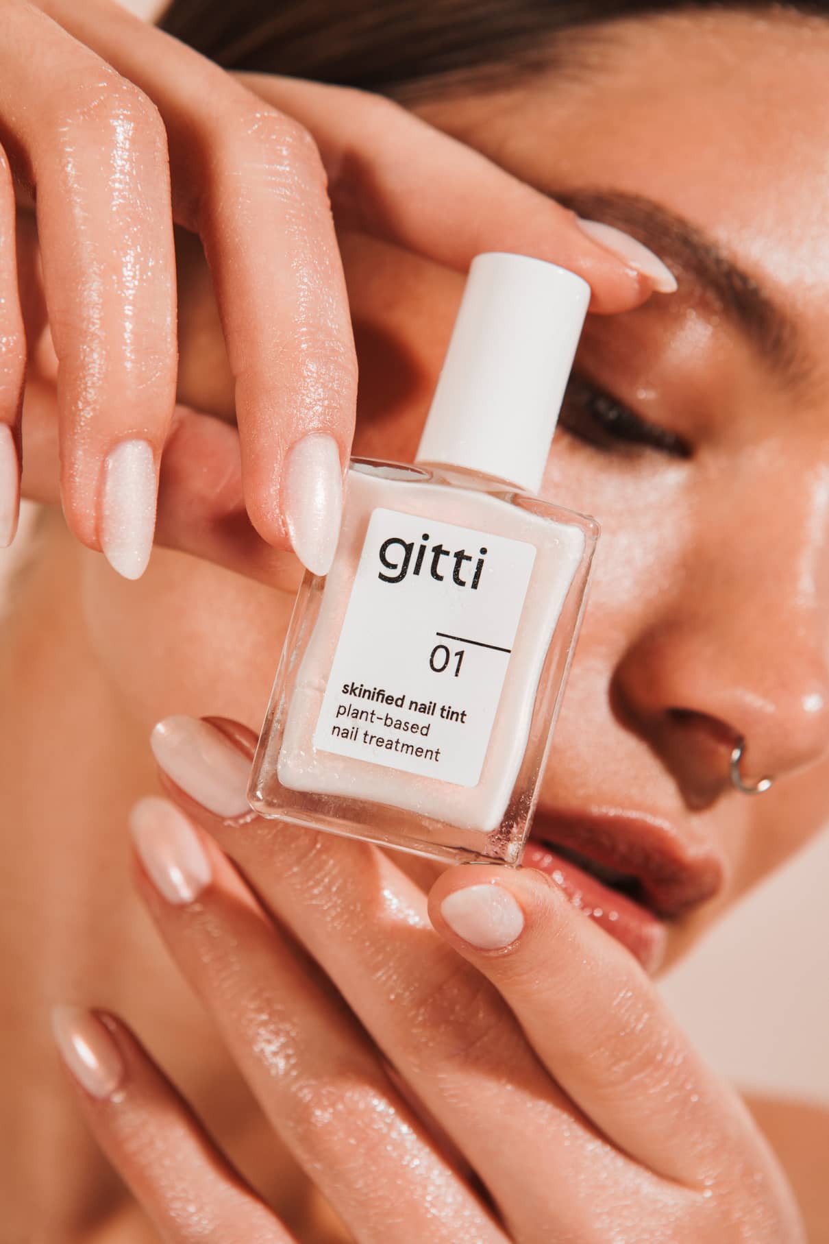 Close up of glossy pale pink nails holding a Skinified Nail Tint 01 bottle.