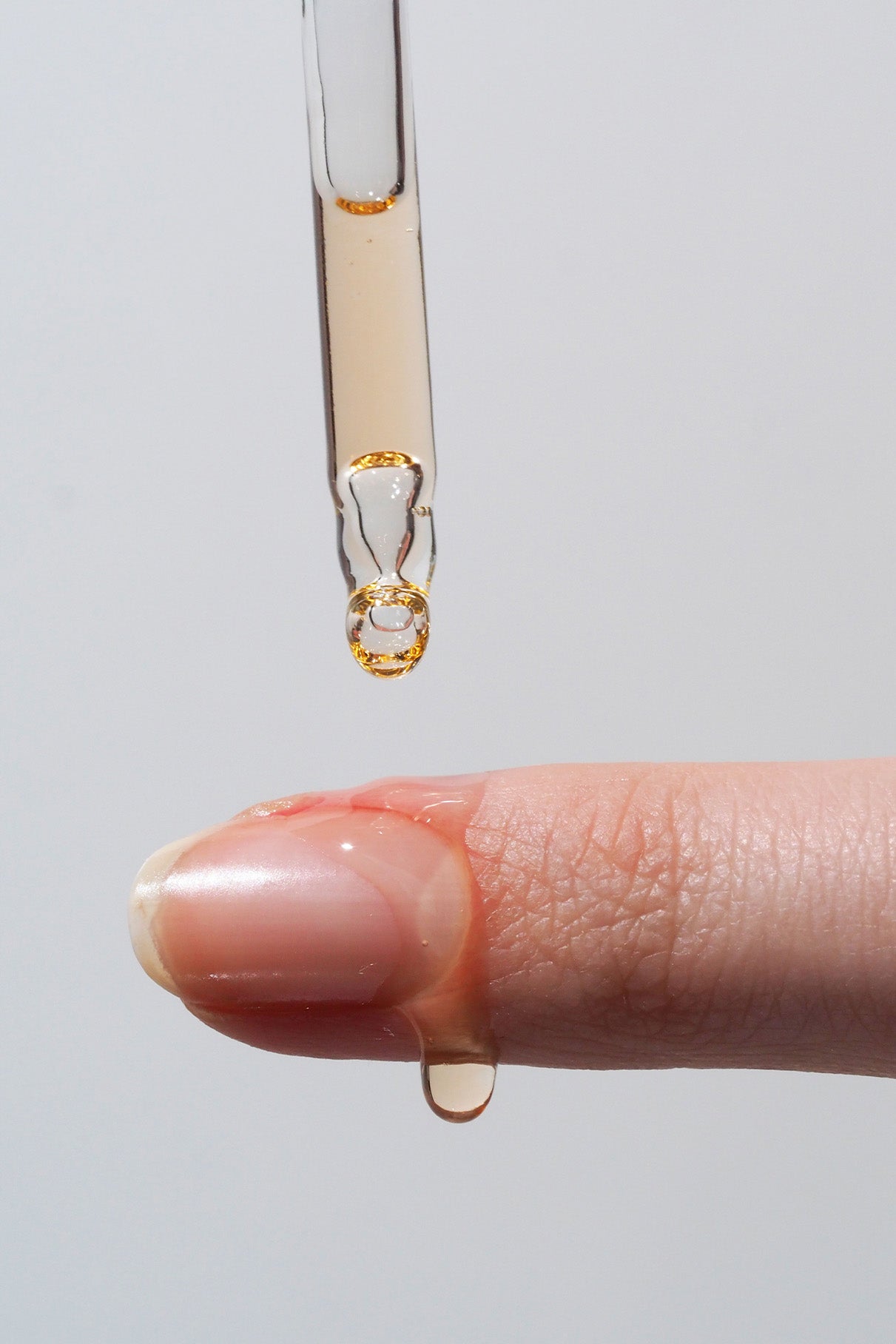 Mit einer Pipette wird Flüssigkeit auf die Spitze eines ausgestreckten Fingers aufgetragen, wobei sich etwas Öl auf dem Nagel sammelt und an der Seite herunterläuft – der perfekte Schliff für ein hochglänzendes Finish und einen Gel-Look in Salonqualität im Rahmen Ihrer „Treat & Gloss“-Routine.