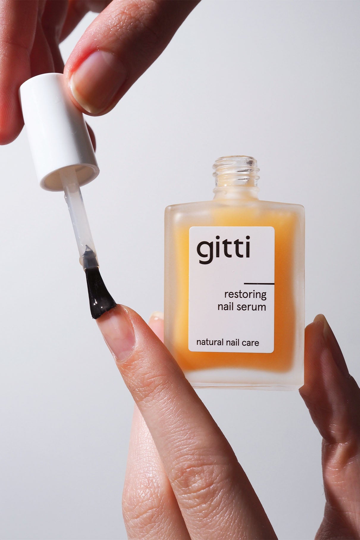 Eine Hand verwendet das Nail Recovery Starter Treatment mit einem Pinselapplikator auf einem Fingernagel, um die Nägel mit Feuchtigkeit zu versorgen und zu regenerieren. Auf dem Etikett steht "Natural Nail Care".
