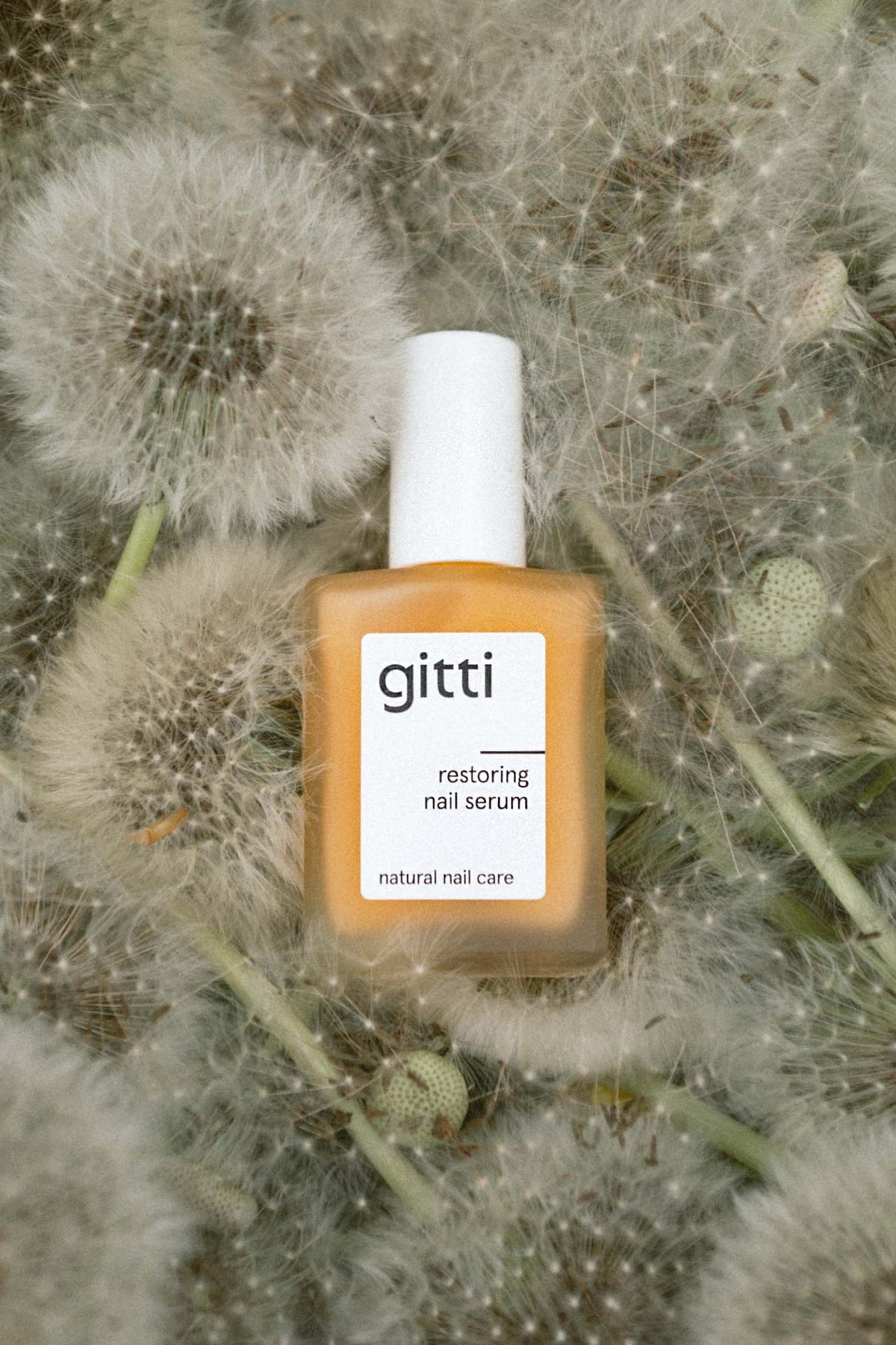 gitti restoring nail serum bottle in orange among dandelion seed heads