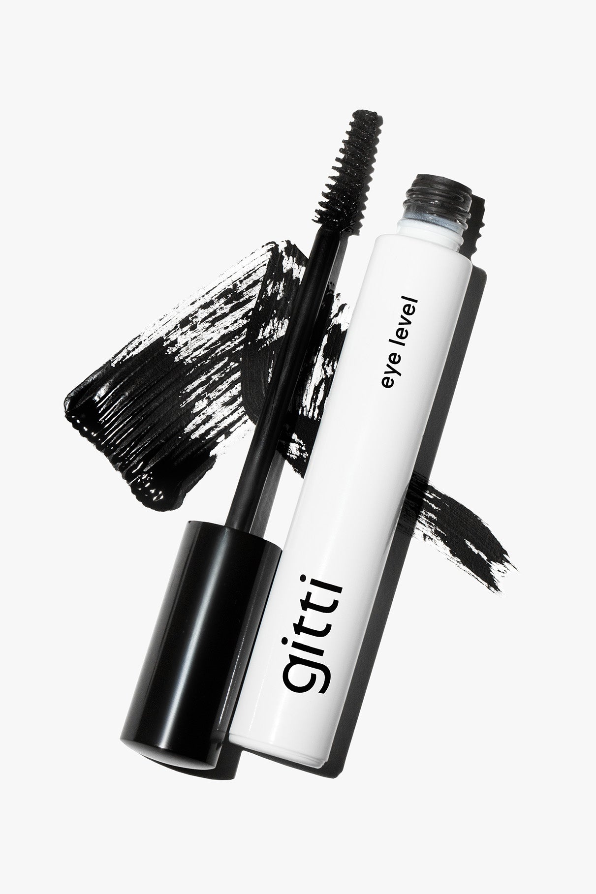 Eine Mascara-Tube aus dem Lash, Lip & Cheek Trio mit abgenommenem Stift liegt auf einem schwarzen Mascara-Muster vor weißem Hintergrund.