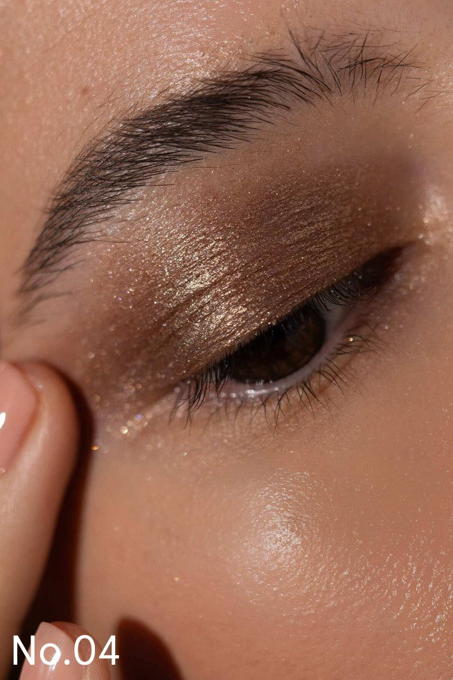Nahaufnahme eines geschlossenen Auges mit braun und gold schimmerndem Lash, Lip & Cheek Trio, gepflegter Augenbraue, glatter Haut und einem Finger auf der Wange. Der Text "No. 04" erscheint in der unteren linken Ecke.