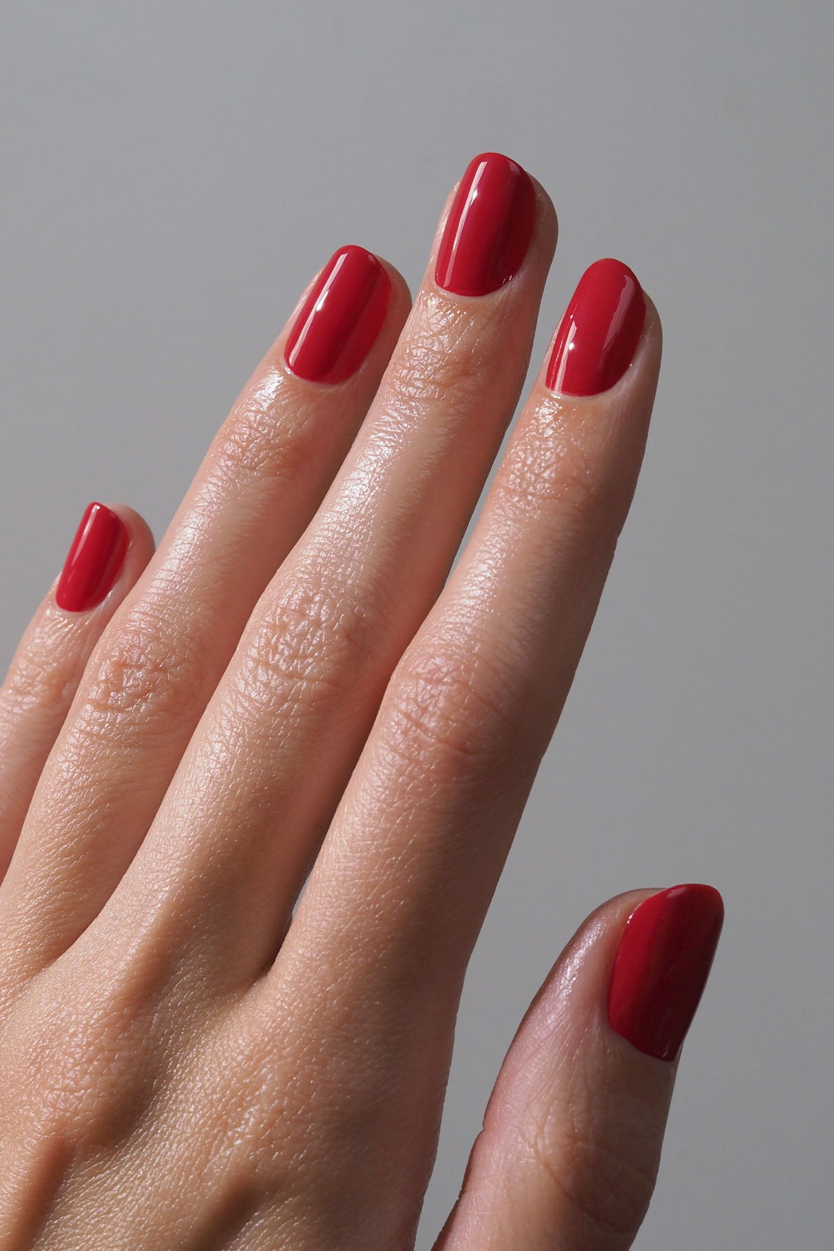 Eine Hand mit sauber manikürten Nägeln, lackiert in glänzendem Rot aus dem Mini Getaway Set, abgeschlossen mit Top & Base Coat, vor einem schlichten hellen Hintergrund.