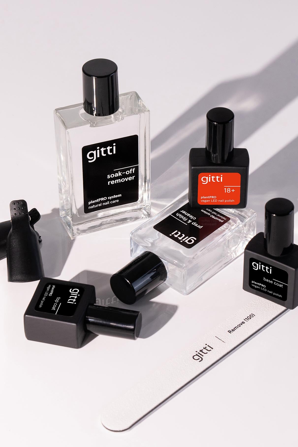 Das plantPRO Essentials Set enthält fünf Nagelpflegeflaschen mit schwarzem Verschluss, einen Base Coat, eine weiße Nagelfeile und zwei schwarze Lackflaschenhalter, die auf einer weißen Fläche angeordnet sind.