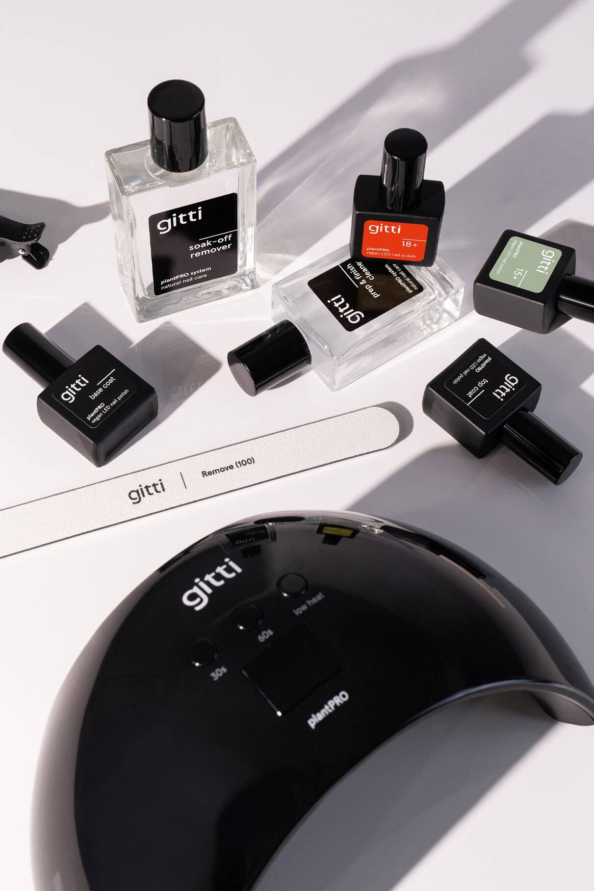 Verschiedene Gitti-Nagelprodukte, darunter Nagellackflaschen, eine Nagelfeile und das plantPRO System + Lampe, sind auf einer weißen Fläche angeordnet.