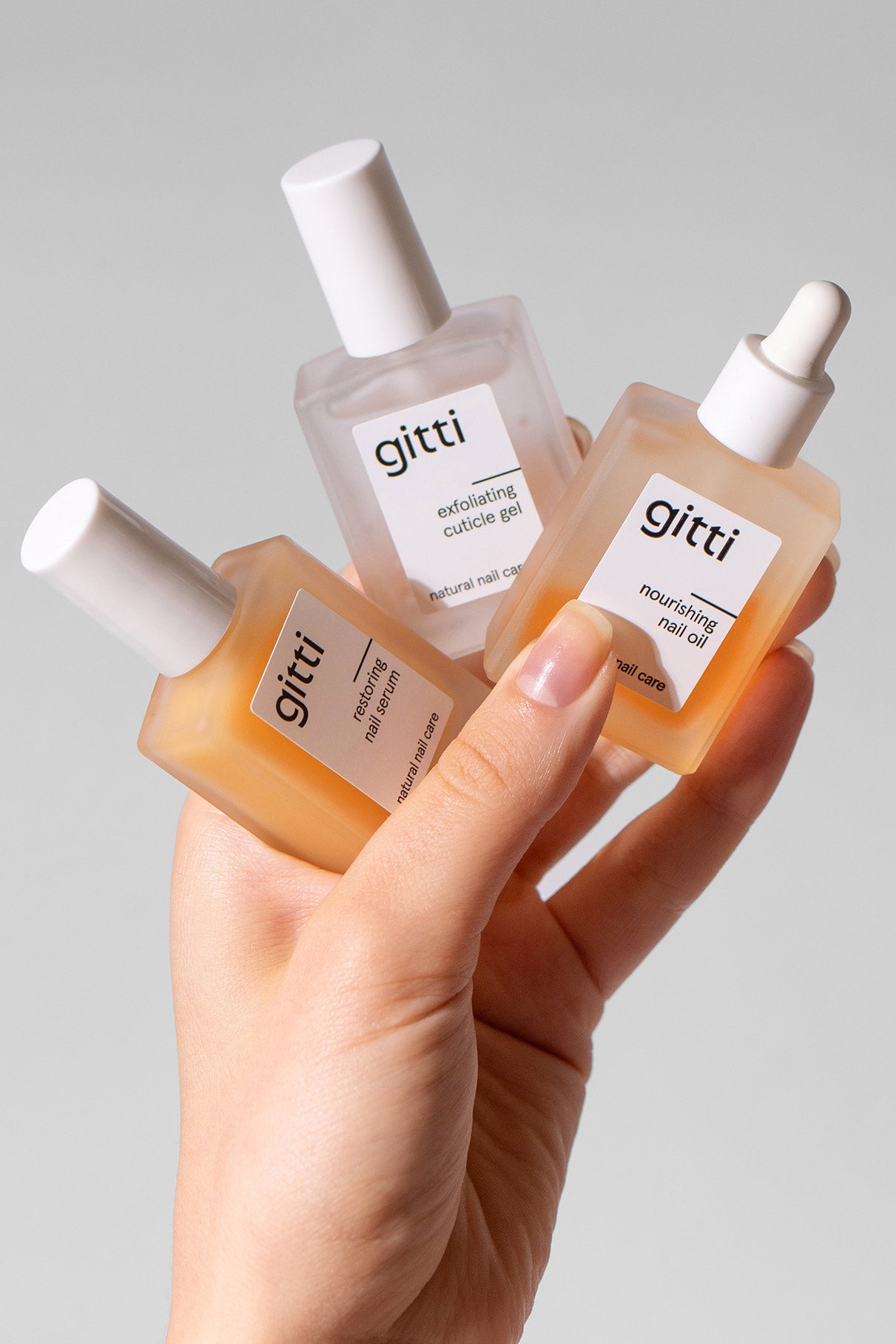Eine Hand hält die Community Box - drei Gitti Nagelpflegeprodukte in Glasflaschen: Peeling-Häutchen-Gel, Nagel-Essenz und pflegendes Nagelöl mit weißem Verschluss. Jetzt Community Box mit kostenlosem Versand sichern!.