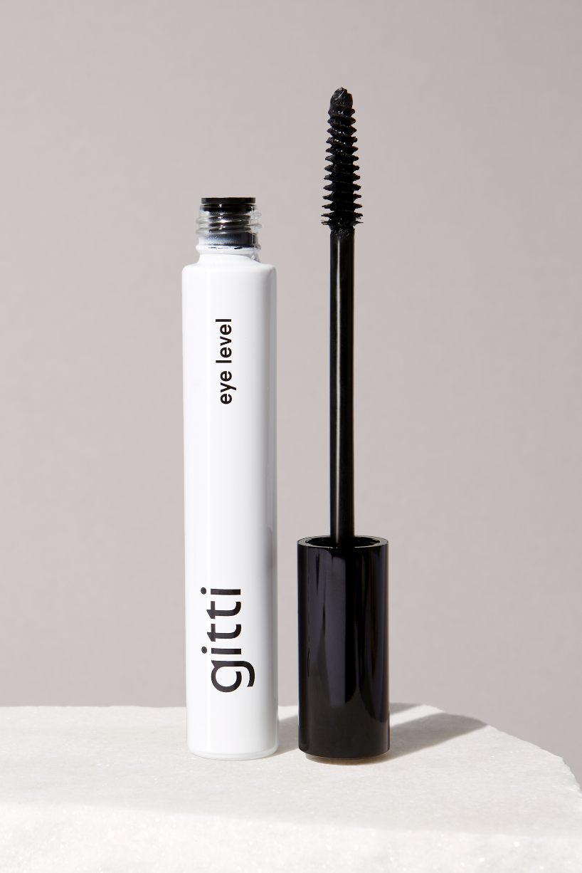 Eine geöffnete Tube Lash Duo Mascara ist abgebildet, wobei der Zauberstab aufrecht neben dem weißen Behälter vor einem neutralen Hintergrund steht.