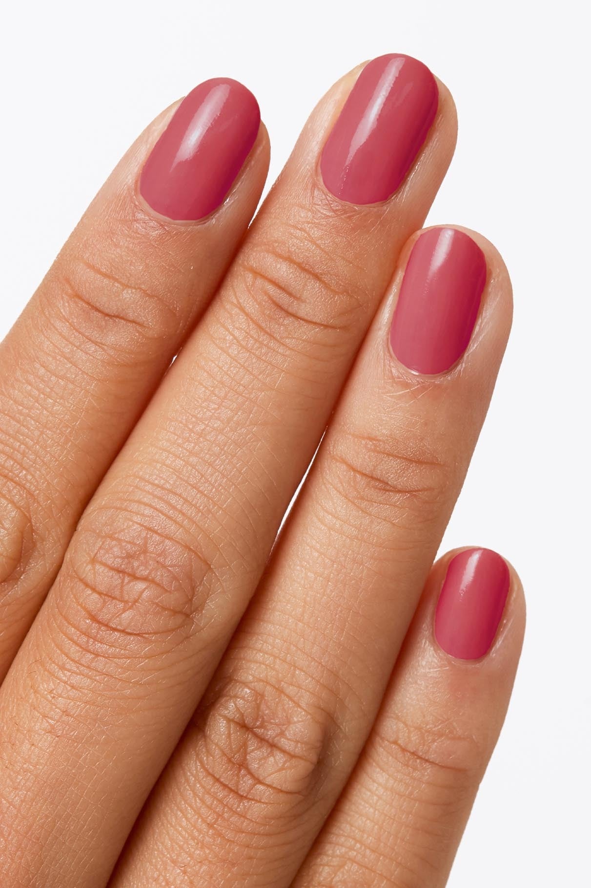 Eine Hand mit Naturnägeln, die in dem glänzenden Rosaton von Nails + Lips in Sync lackiert sind, leuchtet vor einem unifarbenen Hintergrund.