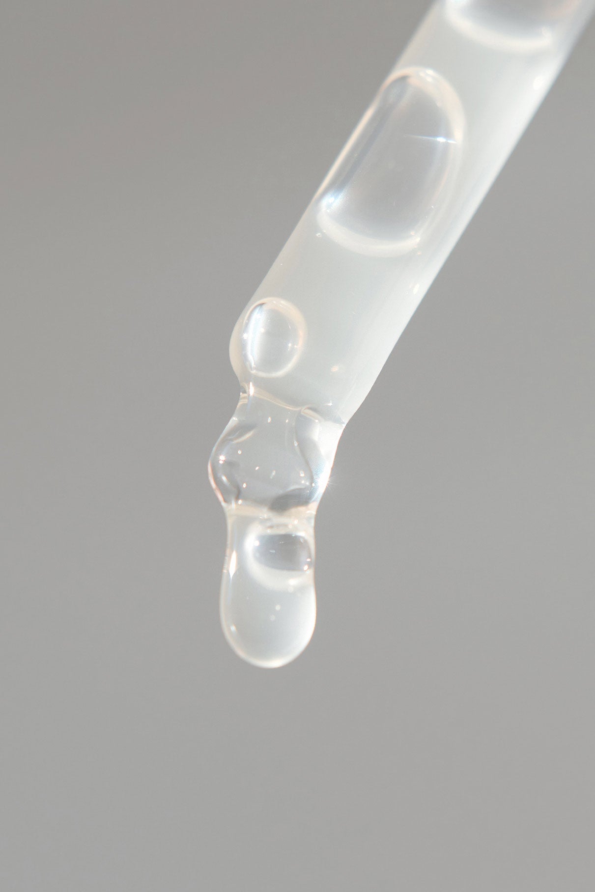Eine Nahaufnahme eines Glastropfers aus dem Serum-Duo-Set setzt eine klare, zähflüssige Flüssigkeit vor einem schlichten, hellgrauen Hintergrund frei.
