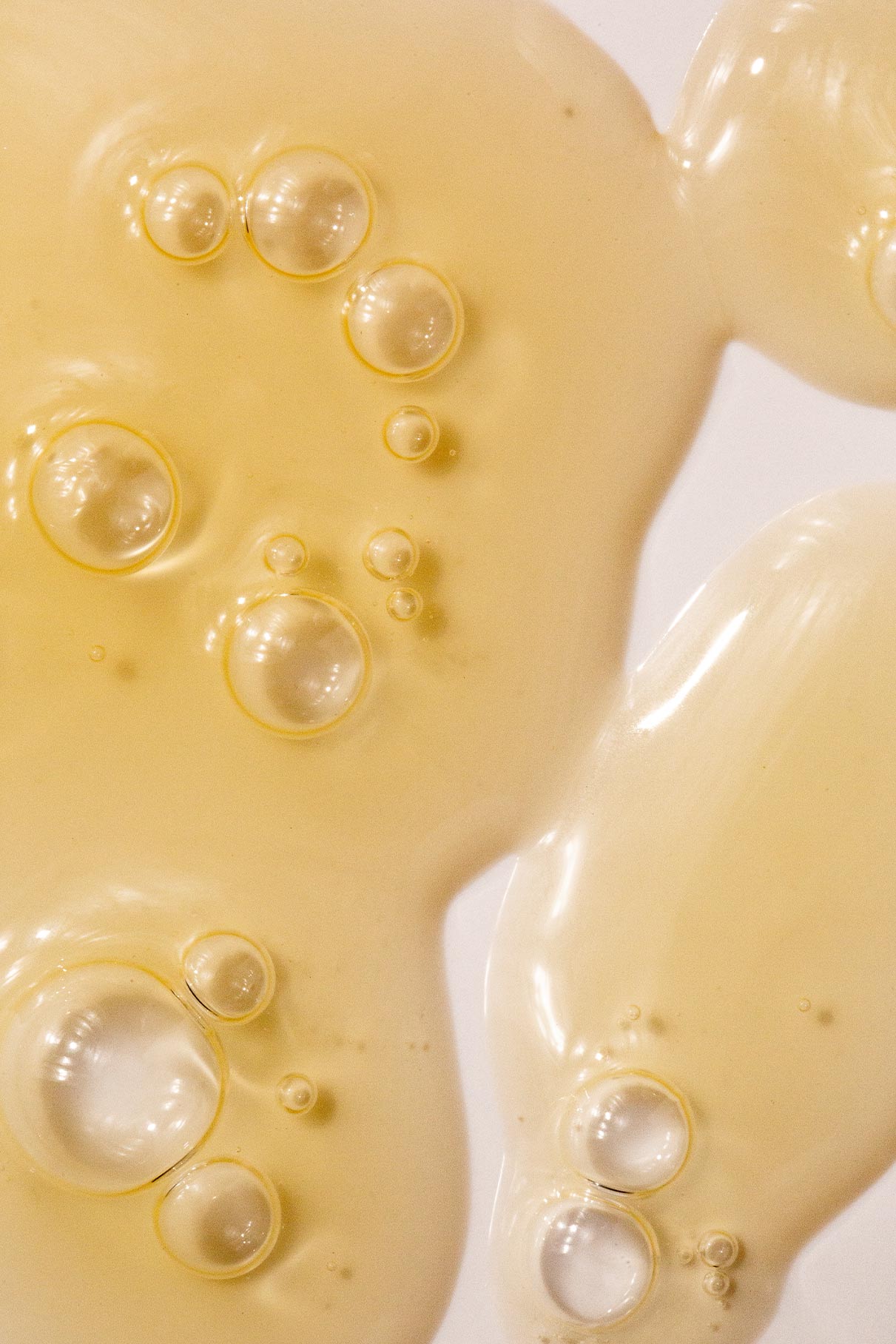 Nahaufnahme einer gelblichen Flüssigkeit mit Blasen auf einem glatten weißen Hintergrund, die die Textur und Klarheit widerspiegelt, die mit dem Ease-and-Even-Serum erreicht wurde - ideal zum Ausgleich der Talgproduktion und zur Behandlung von Hautunreinheiten.