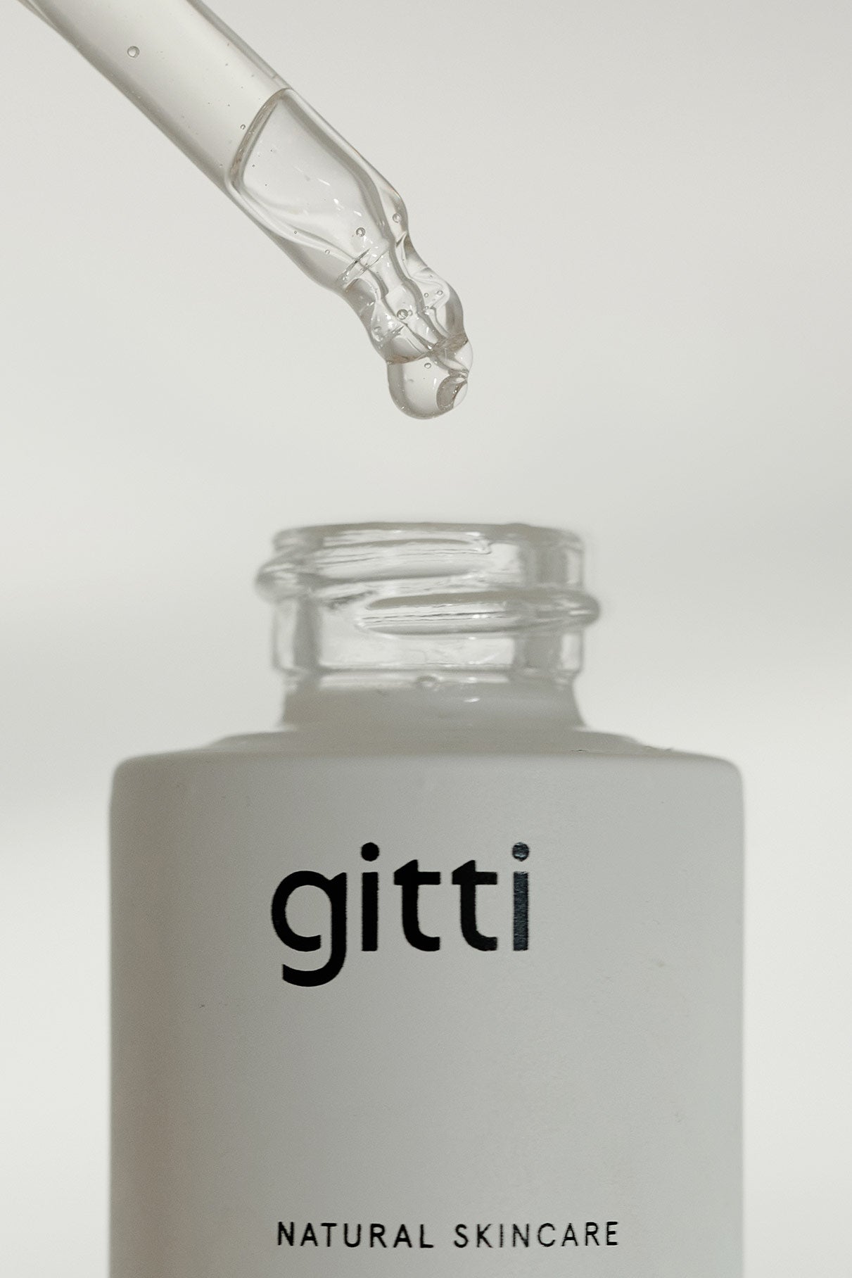 Ein Glastropfer spendet Flüssigkeit über einer offenen weißen Flasche mit der Aufschrift Glow-And-Protect Serum, das Feuchtigkeit spendet und vor blauem Licht schützt, vor einem schlichten Hintergrund.