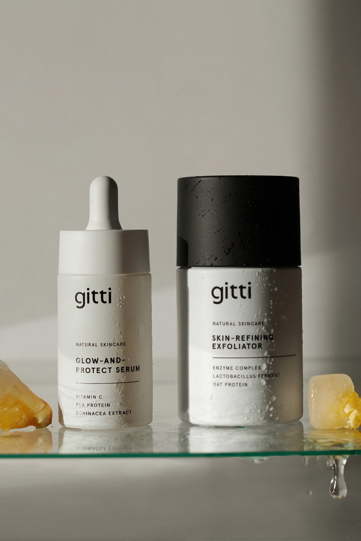 Das Ultimate Glow Duo wird Seite an Seite mit Wassertropfen und teilweise geschmolzenen Eiswürfeln auf einer Glasfläche präsentiert.