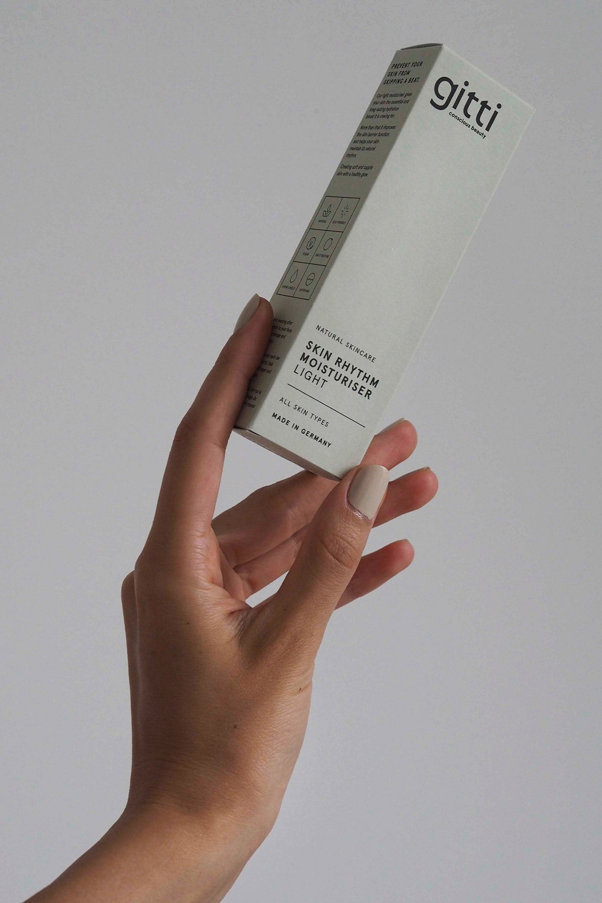 Eine Hand hält eine Dose Skin Rhythm Moisturiser Light vor einem schlichten hellgrauen Hintergrund - Ihre erste Wahl, wenn es um Feuchtigkeitspflege und Barriereschutz für lang anhaltenden Glanz geht.