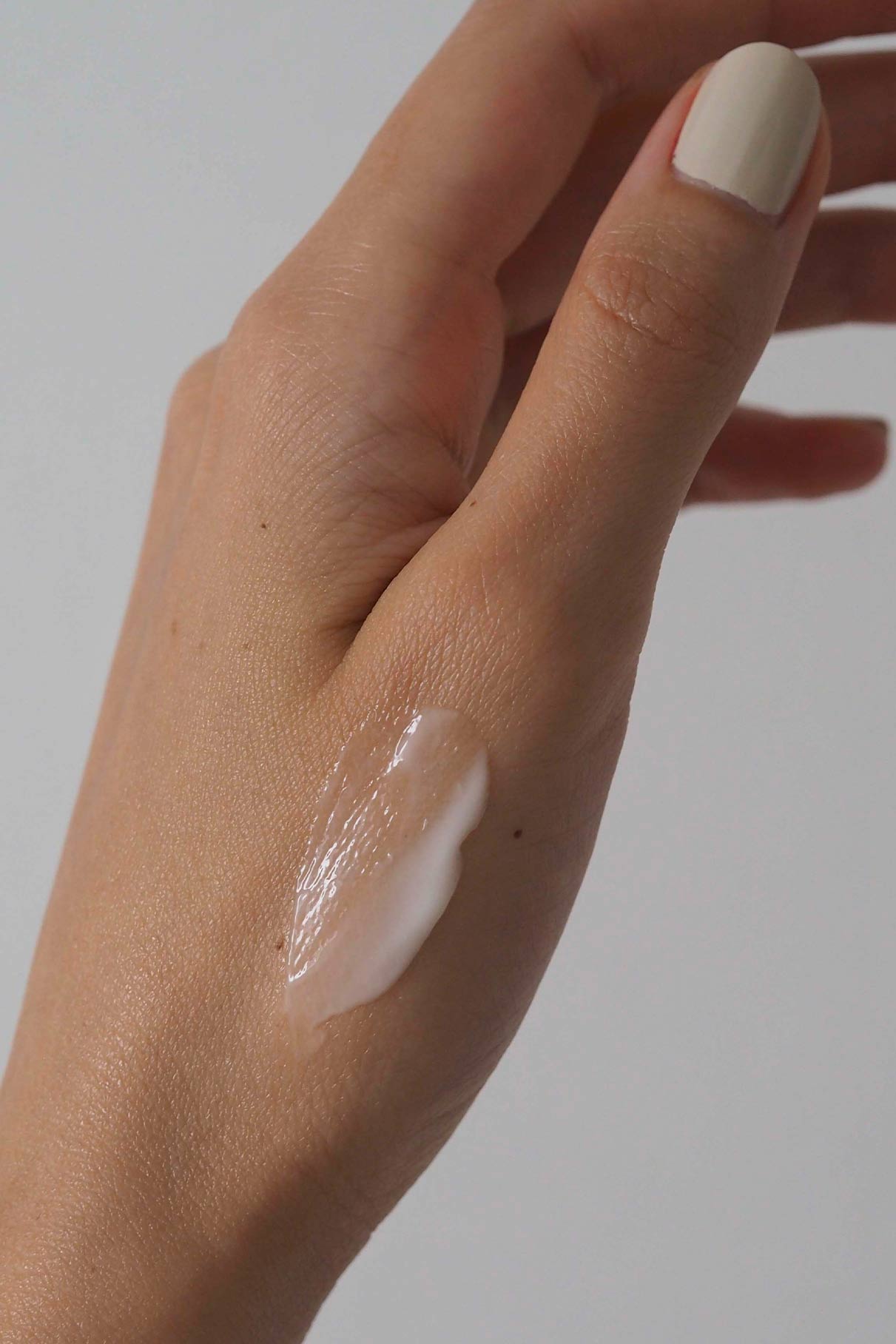 Eine Hand mit hellem Nagellack trägt auf dem Handrücken Skin Rhythm Moisturiser Light, der den Barriereschutz und die zusätzliche Feuchtigkeit betont, vor einem schlichten Hintergrund.