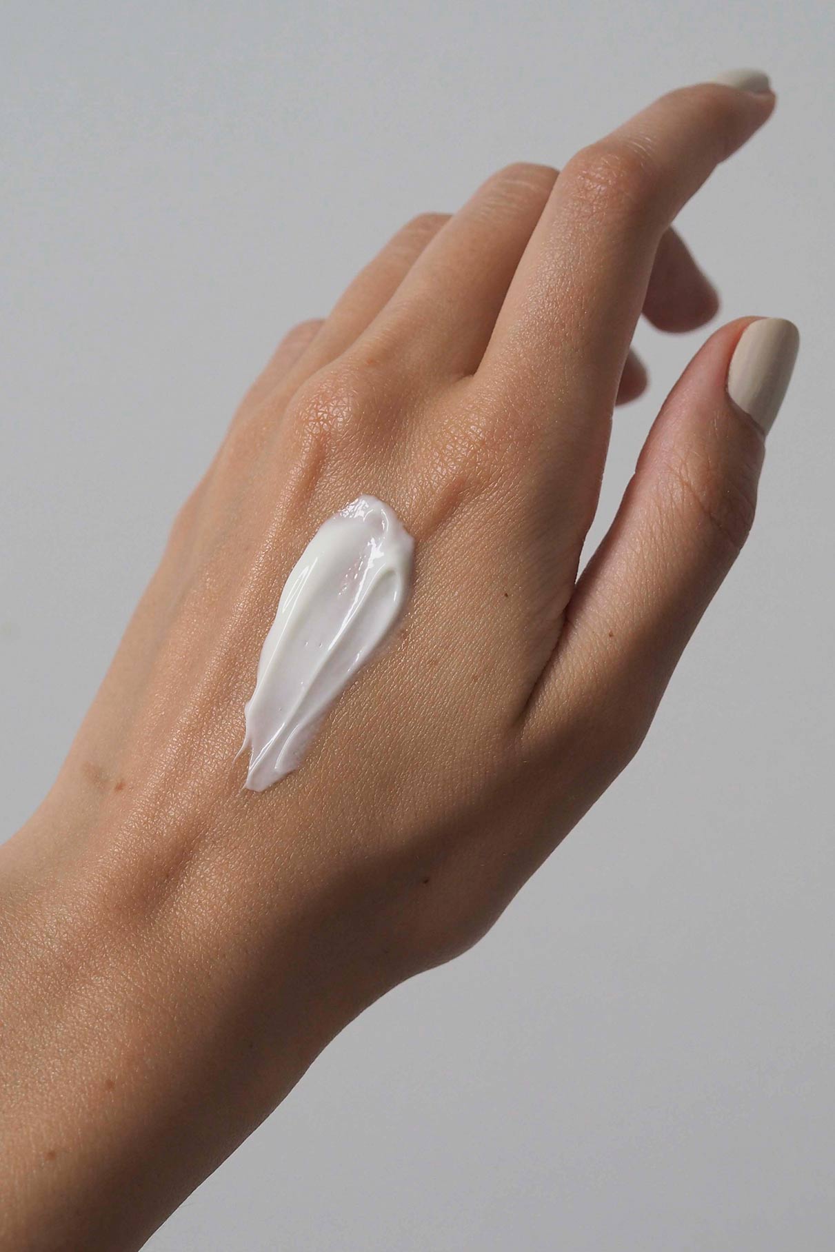 Eine Hand mit hellem Hautton zeigt einen Streifen Skin Rhythm Moisturiser Rich auf dem Rücken, der die Feuchtigkeitspflege und den Barriereschutz betont, vor einem schlichten hellgrauen Hintergrund.